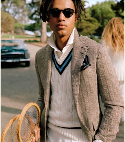 Man wears cable-knit cricket sweater under grey blazer.