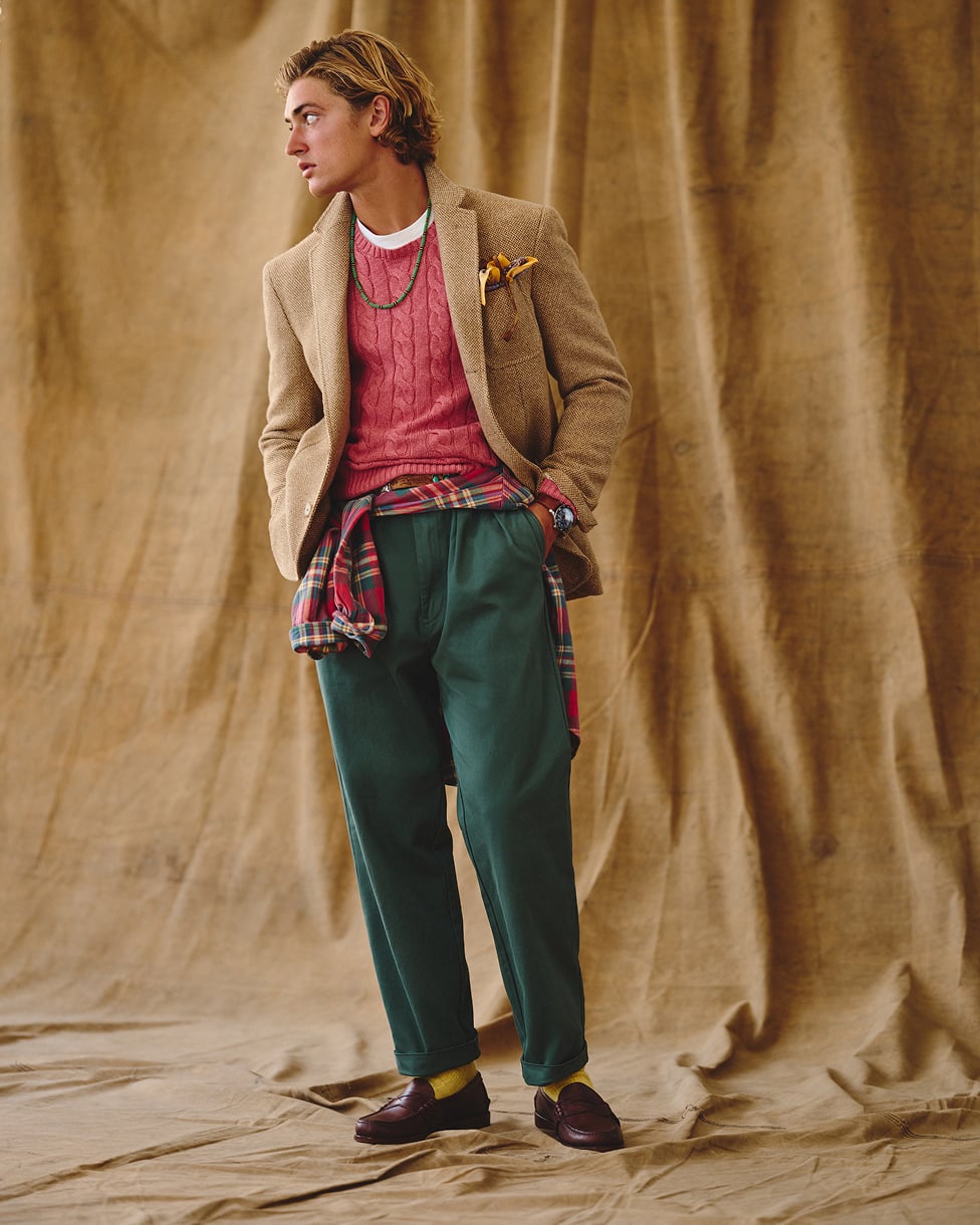 Homem com camisola vermelha, blazer bege, calças de ganga e mocassins.